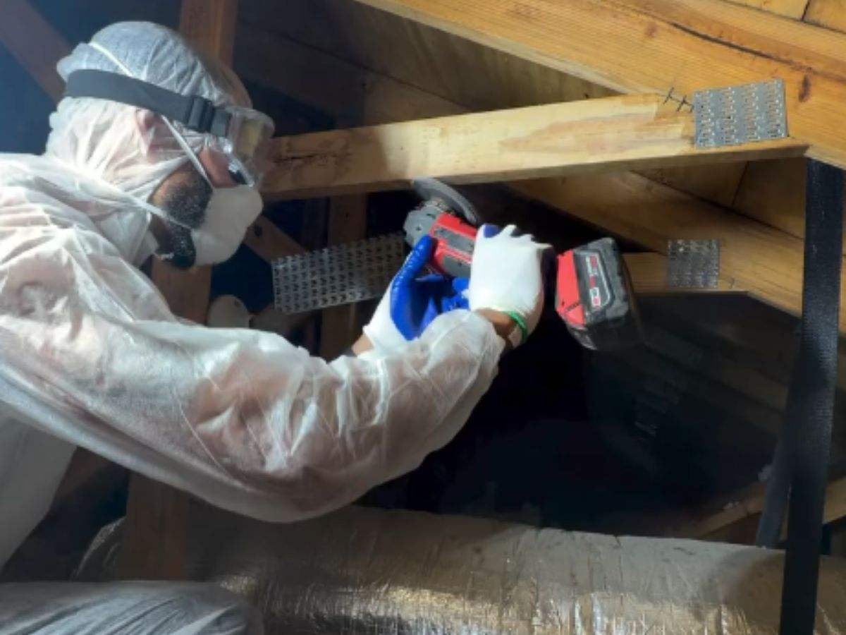 Technician in a protective suit, goggles and respirator working on attic truss framing